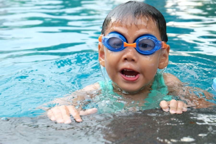 Kleinkind schwimmt in einem Pool und trägt eine blaue Schwimmbrille
